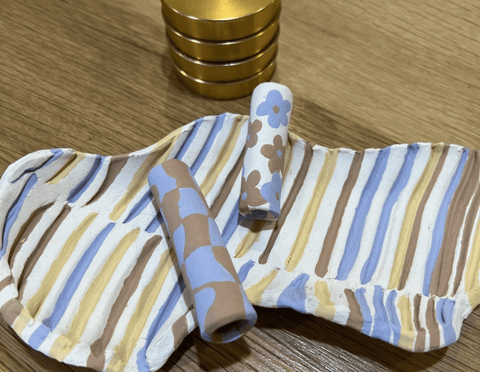 White ceramic rolling tray in blue, brown, yellow stripes with clay chillums and gold grinder